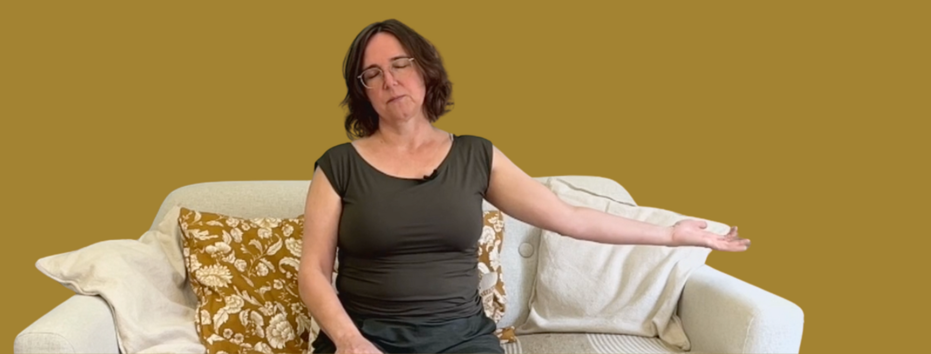 Vrouw zittend op een bank, haar rechterarm uitgestrekt. Gele muur op de achtergrond.