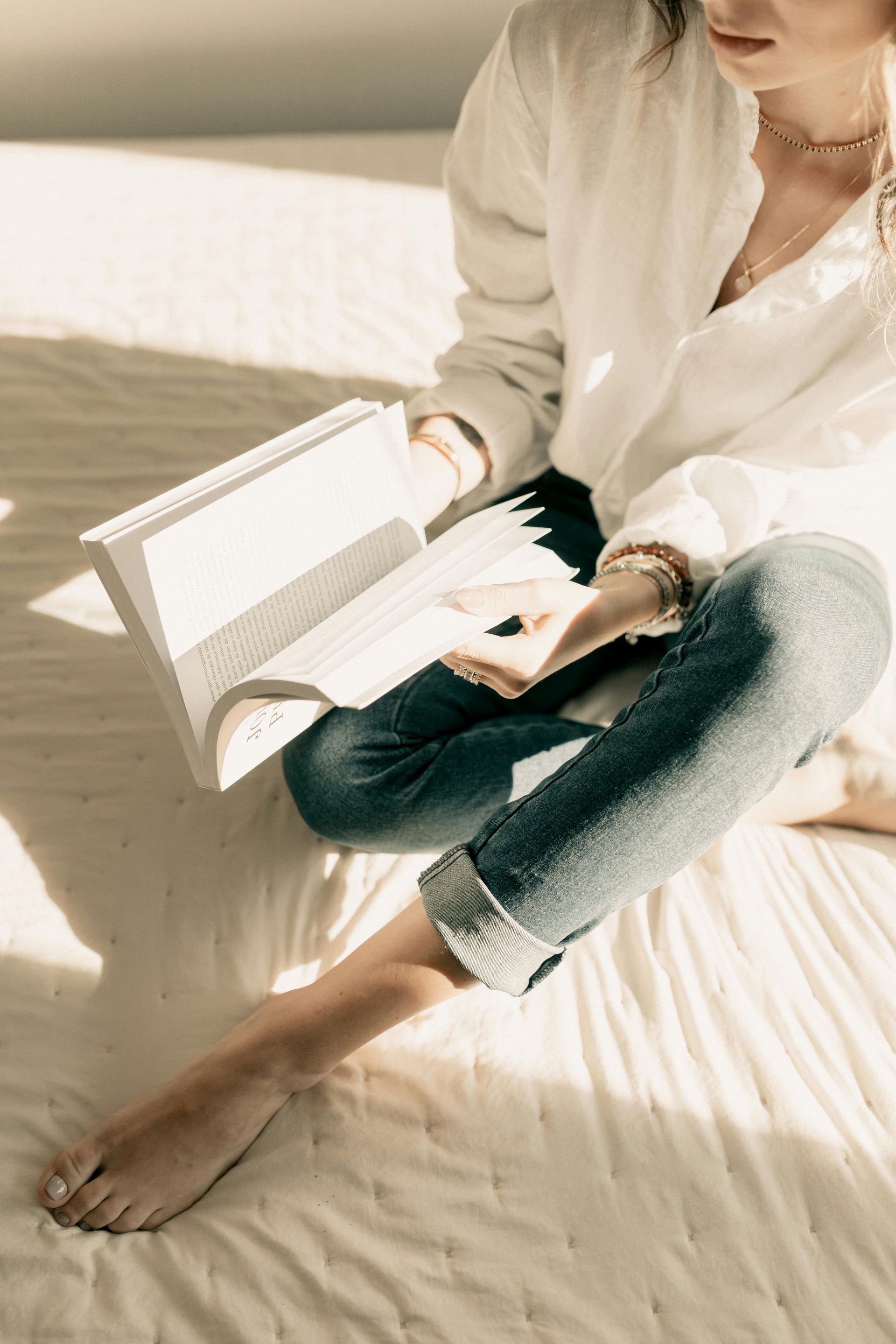 Een vrouw zit op het bed en leest een boek.