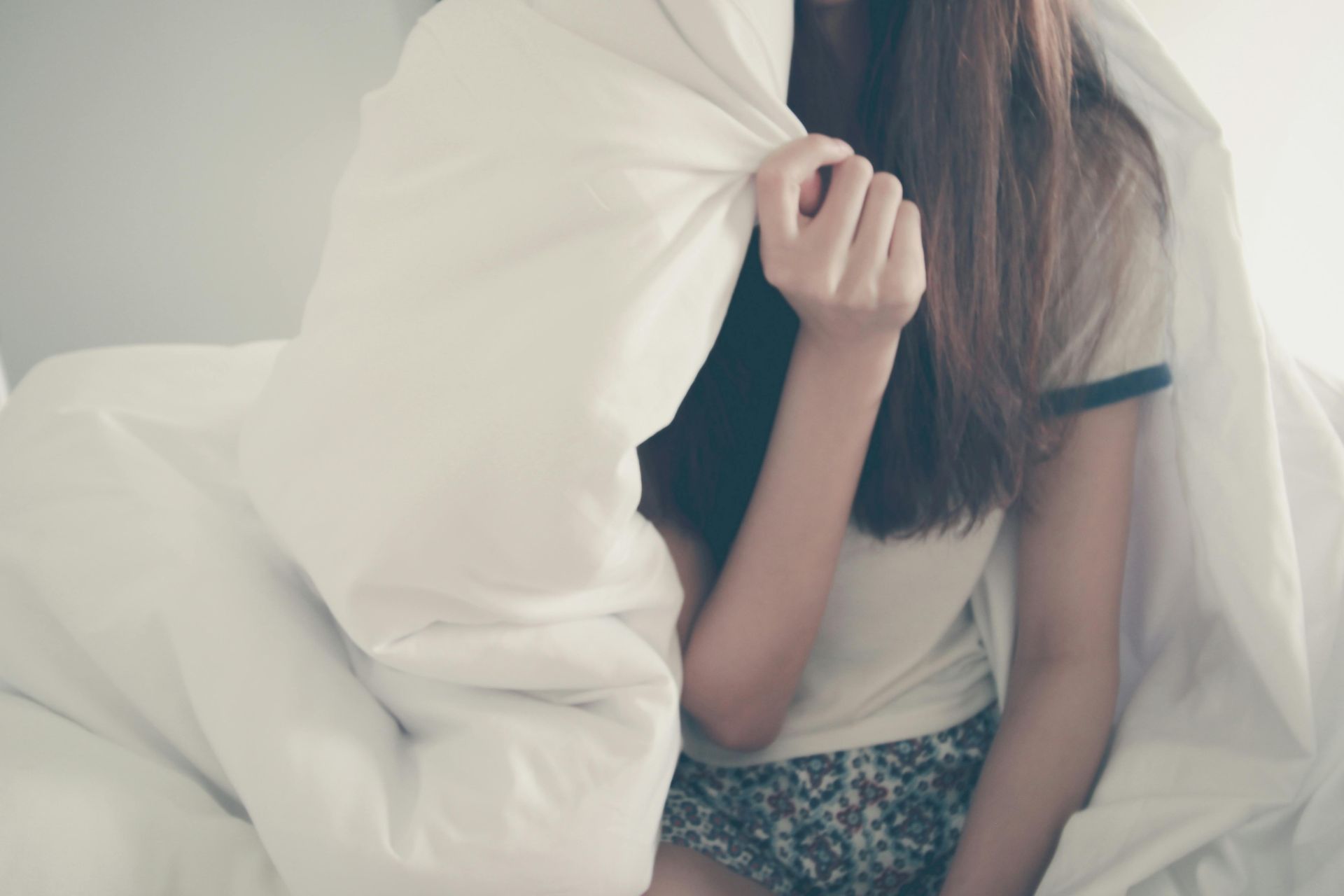 Vrouw in bed, met een witte dekbed over zich heen getrokken.