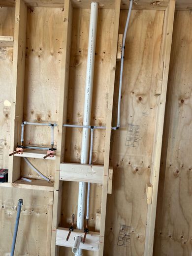 Plumbing and PVC piping installed within the wooden wall studs of a building under construction.