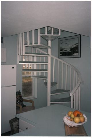 A kitchen with a spiral staircase and a bowl of fruit on a table.