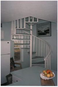 A spiral staircase in a kitchen with a bowl of fruit on the counter