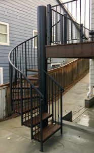 A spiral staircase with wooden steps is outside of a house.