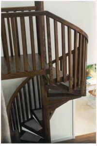 A wooden spiral staircase with a wooden railing in a living room.