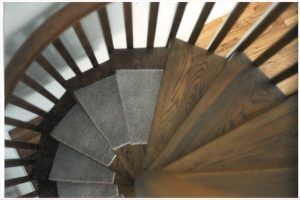 A spiral staircase with a wooden railing and carpeted steps