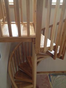 A wooden spiral staircase with a wooden railing in a room.