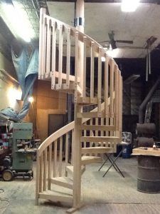 A wooden spiral staircase is being built in a workshop.