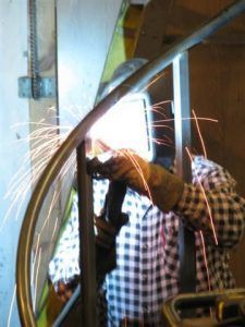 A man wearing a welding mask is welding a metal railing.