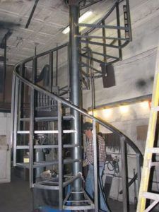 A man is standing next to a spiral staircase in a building.