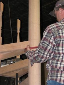 A man in a plaid shirt is measuring a wooden post with a tape measure.