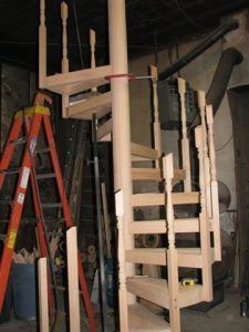 A wooden spiral staircase with a ladder in the background