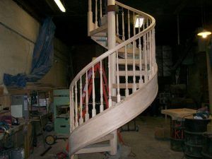 A wooden spiral staircase is being built in a workshop.