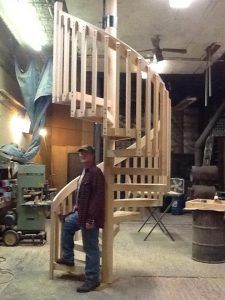 A man is standing next to a wooden spiral staircase in a garage.