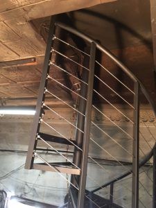 A spiral staircase with a stainless steel railing in a building.