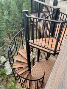 A spiral staircase with wooden steps and a metal railing on a deck.