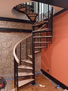 A spiral staircase is sitting in a room next to a brick wall.