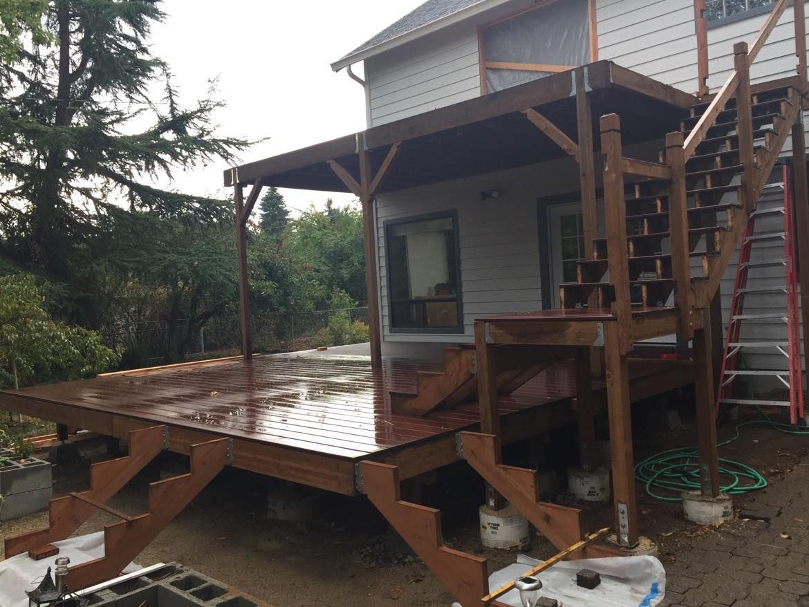 Brown wooden deck with stairs and an overhead roof extension attached to a house.