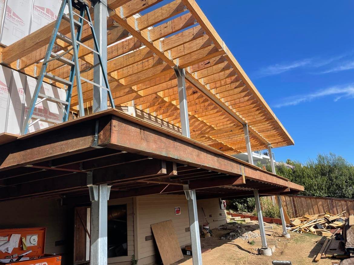 Wooden deck construction with a blue sky background. Supports, framing, and unfinished structure visible.
