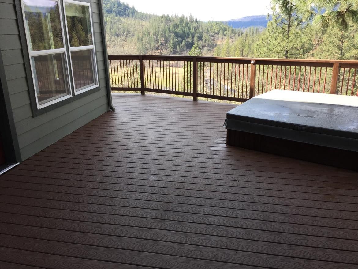 Brown deck with hot tub, railing, and mountain view through windows.