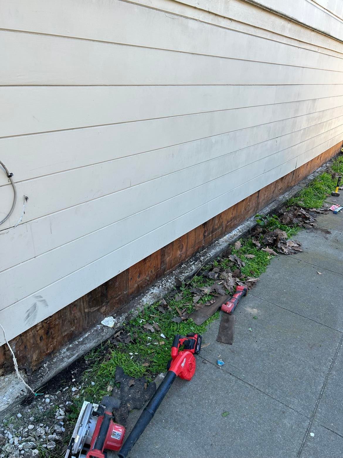 Damaged siding on a building, exposing wood framing and debris along the ground.