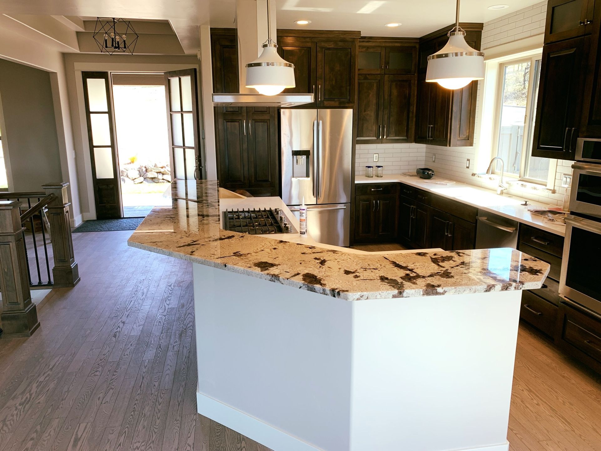 Kitchen with dark wood cabinets, granite countertops, stainless steel appliances, and white pendant lights.