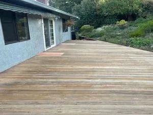 Wooden deck outside a house, with a grassy hillside in the background.