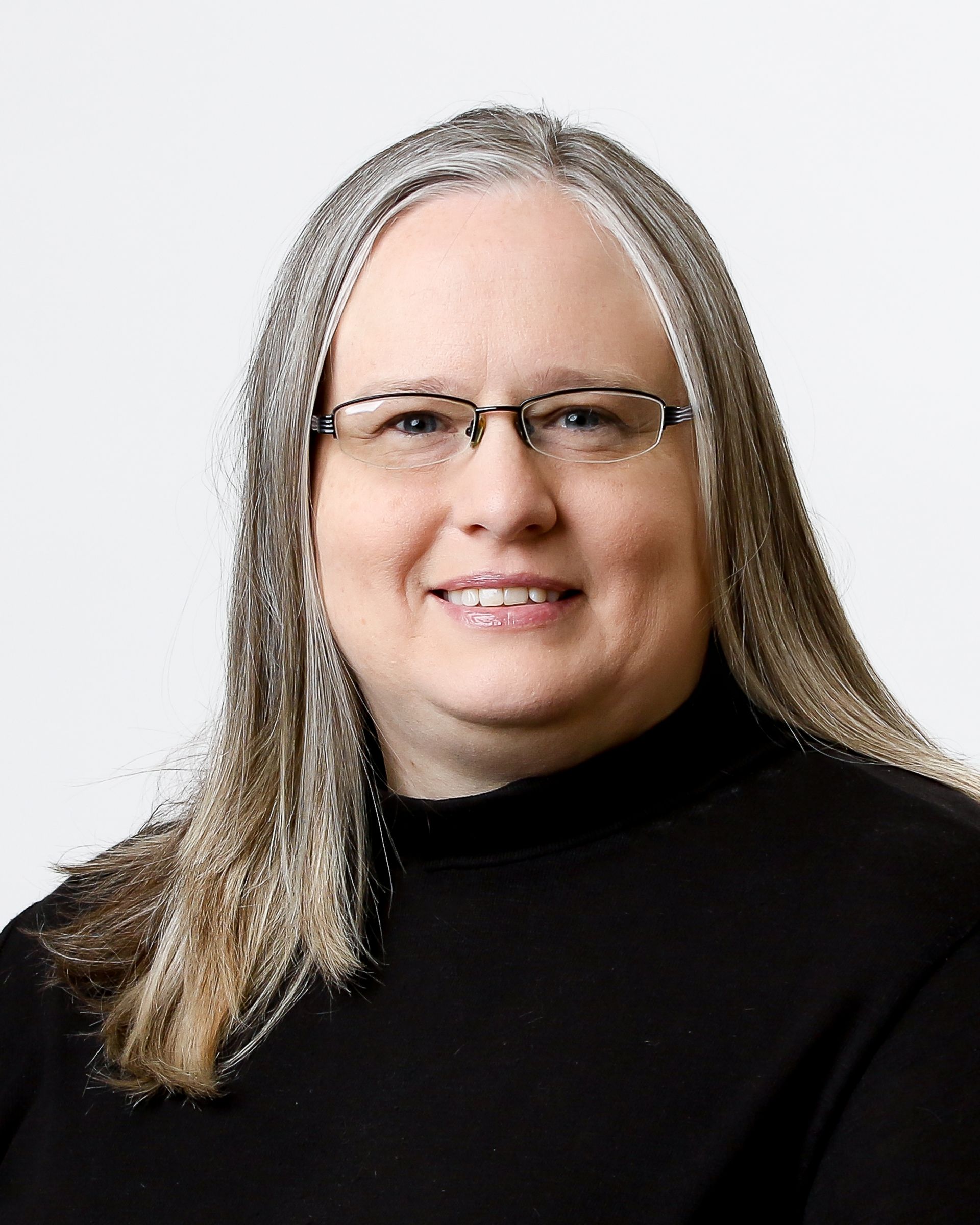 A woman wearing glasses and a black sweater is smiling for the camera.