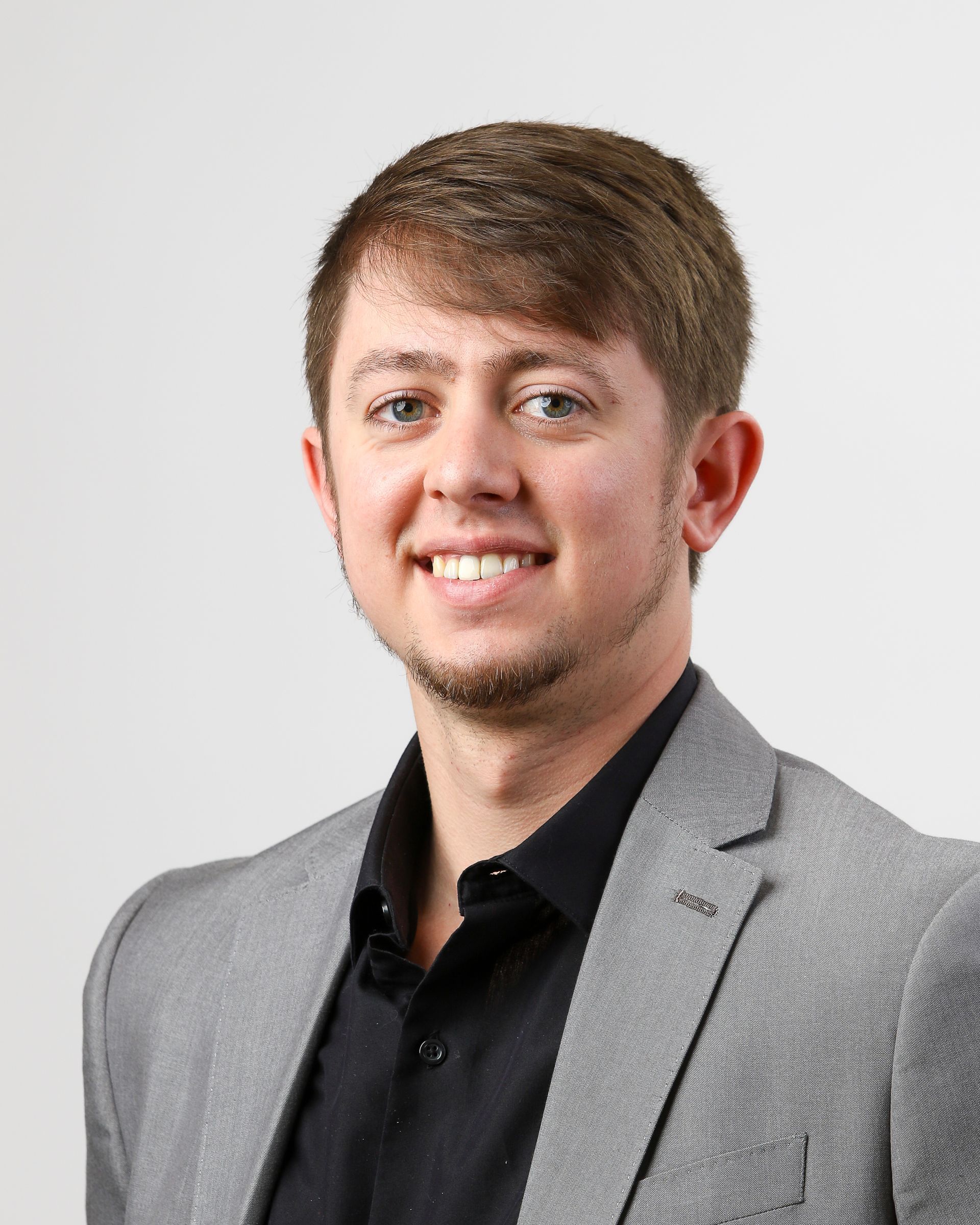A man in a suit and black shirt is smiling for the camera.