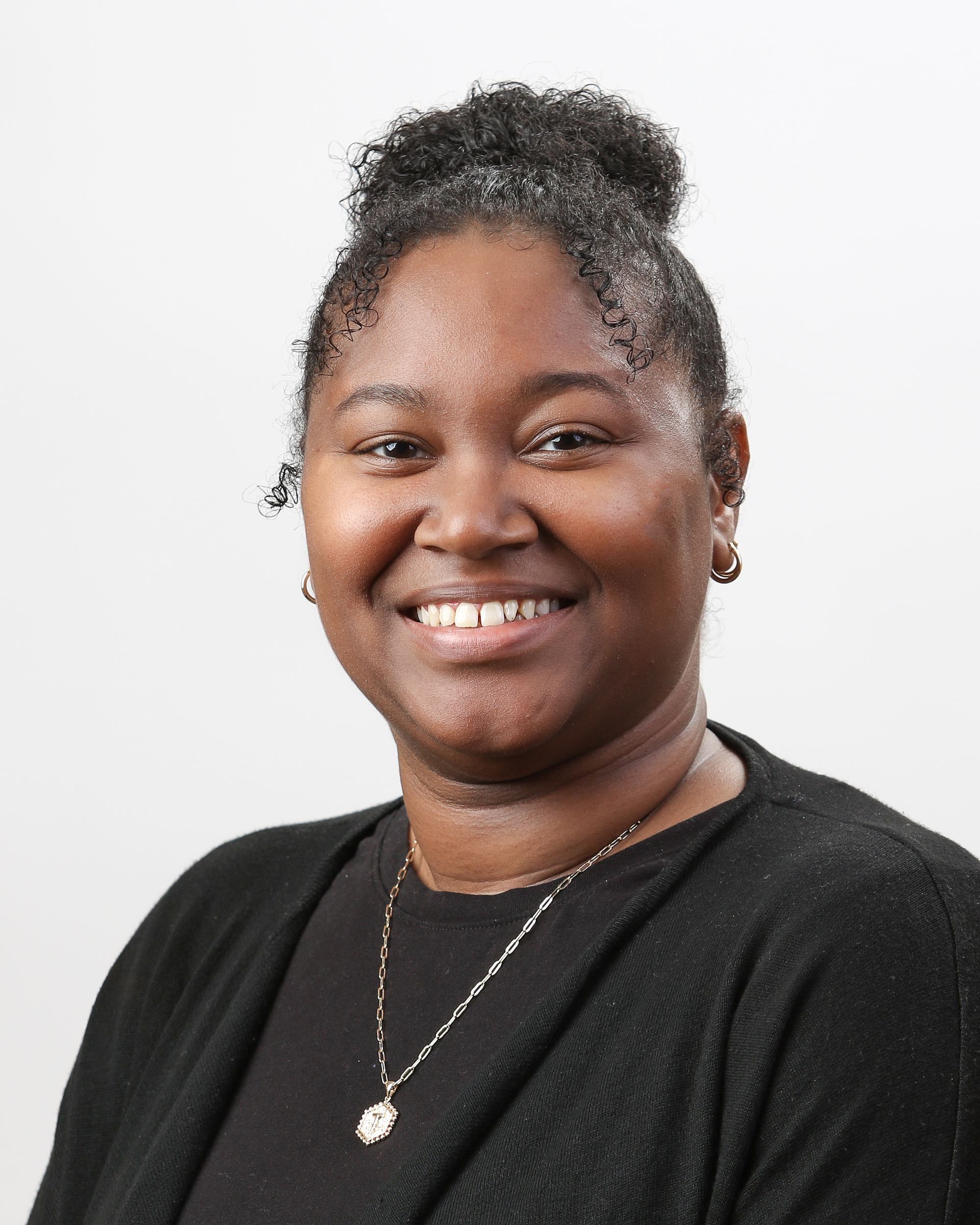 A woman wearing a black sweater and a necklace is smiling for the camera.