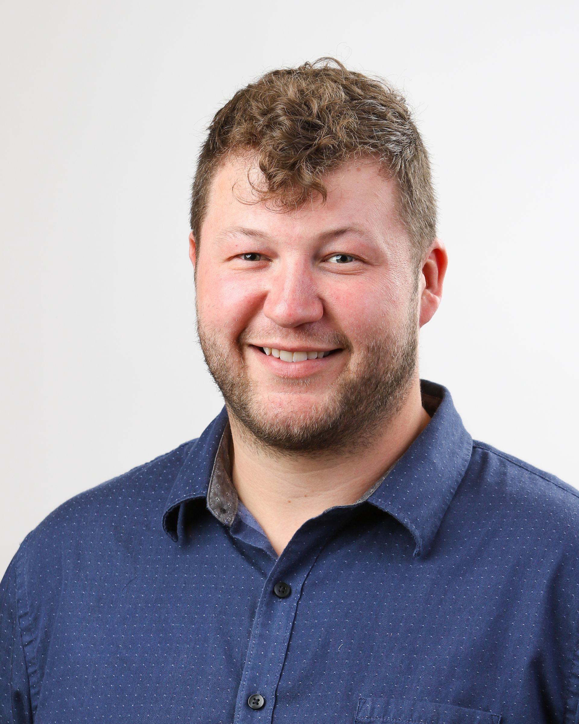 A man with a beard is wearing a blue shirt and smiling.