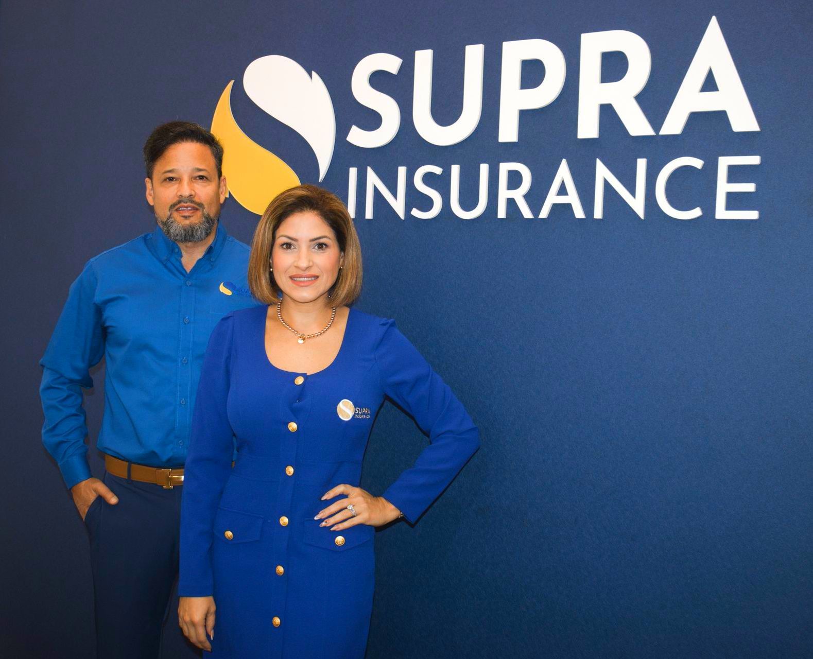 A man and a woman are standing in front of a supra insurance sign.