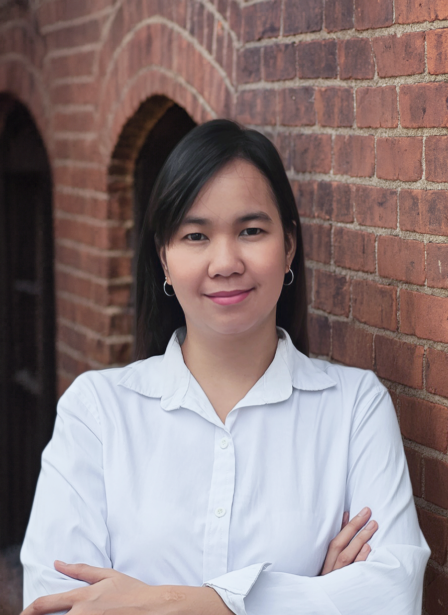 a man wearing glasses and a brown jacket is standing in front of a white brick wall .