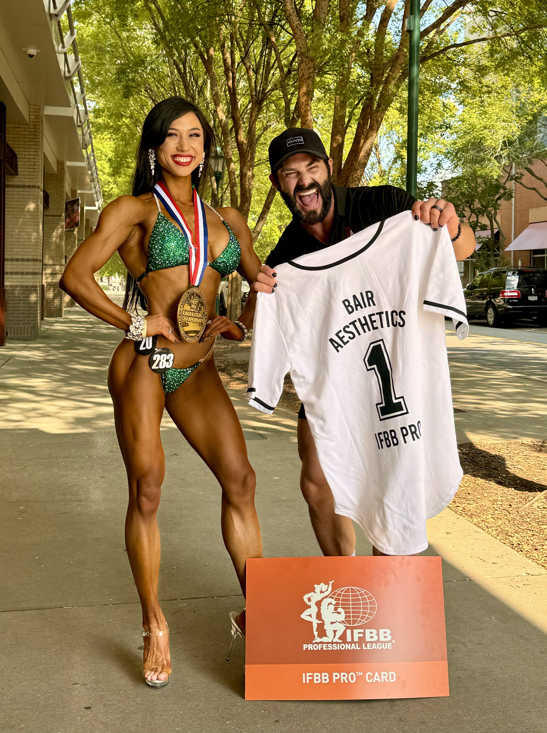 A woman in a bikini is standing next to a man holding a jersey.