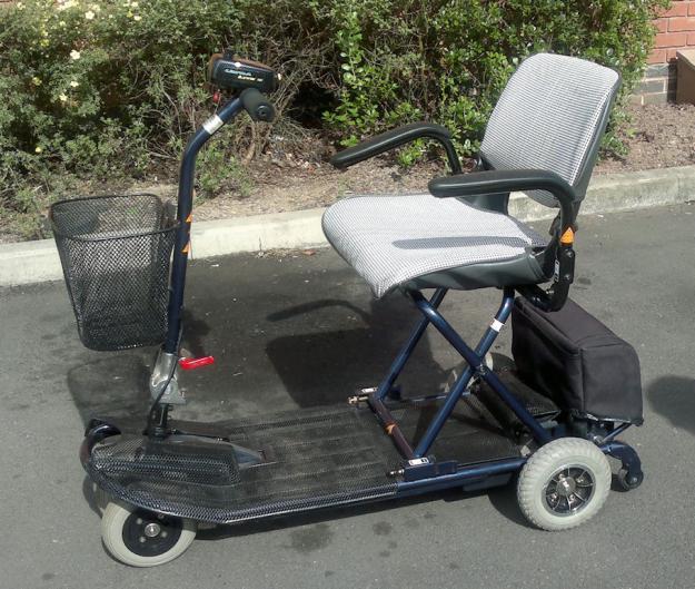 A blue and black mobility scooter with a basket in front, parked on a paved surface.