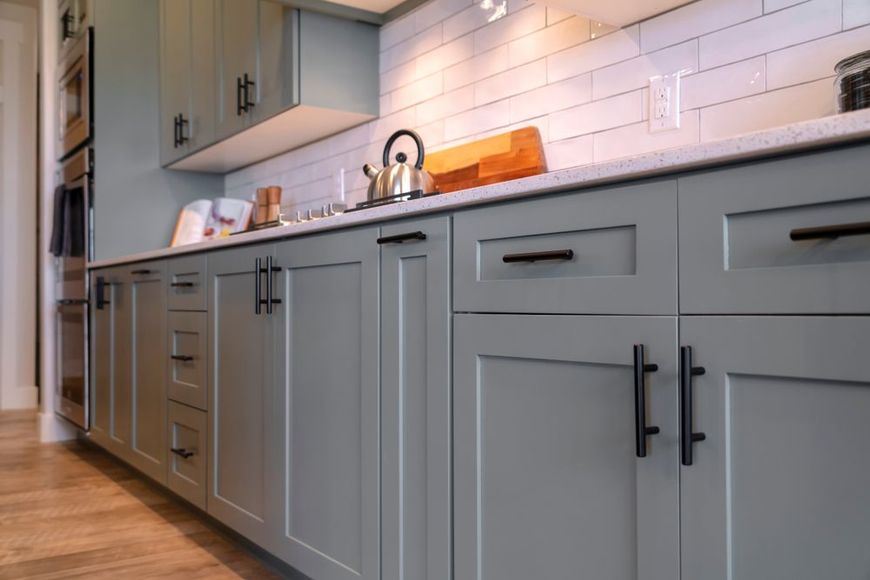 A kitchen with gray cabinets and black handles and a sink.