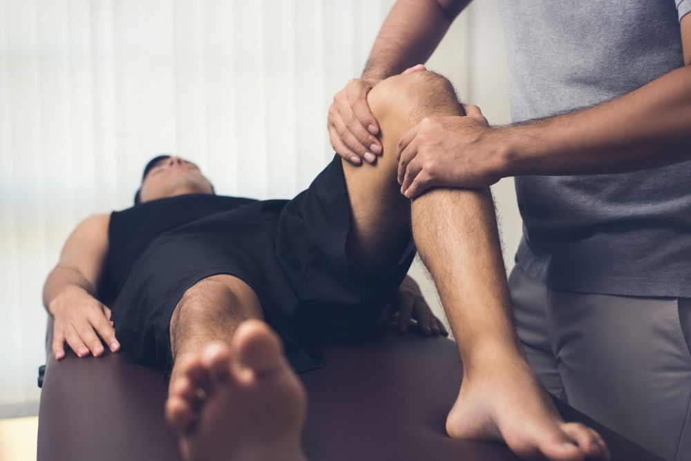 A Man Is Laying On A Table Getting His Knee Examined By A Doctor — A Myo-Therapy Approach To Remedial & Bowen Therapies In West Gladstone, QLD