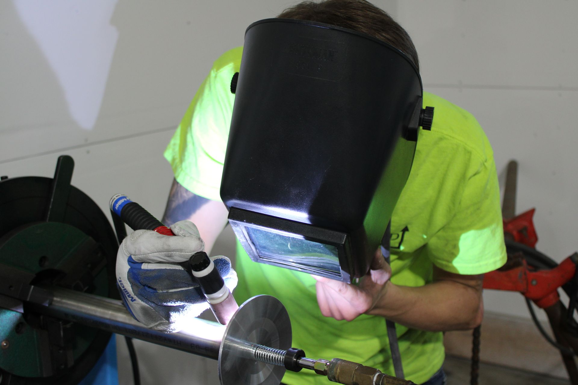 A man wearing a welding mask is welding a piece of metal.