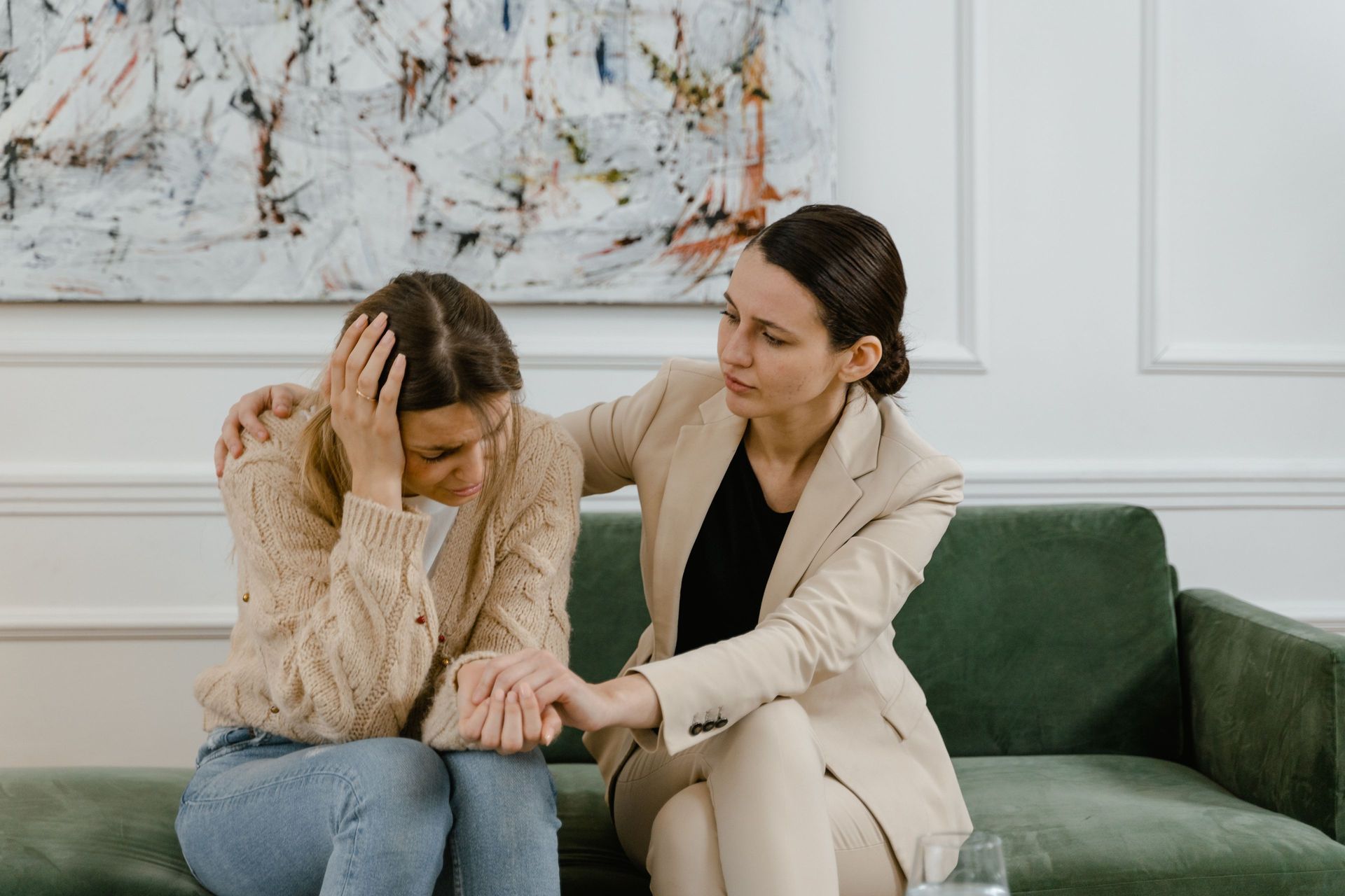 Woman comforted by another; both seated on a green sofa. 