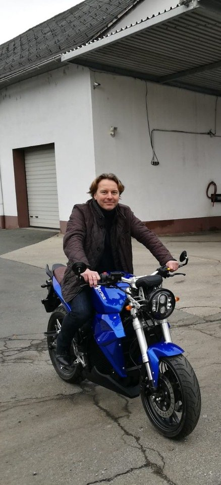 A man is riding a blue electric motorcycle in front of a building. Urban Classic Vienna, Austria 2019