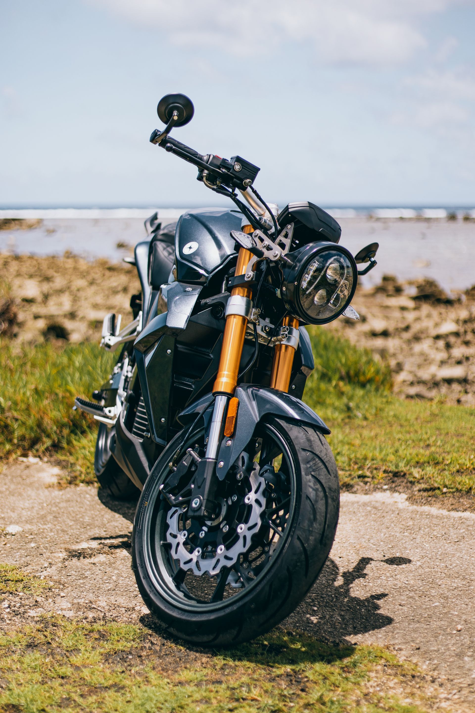 An electric motorcycle is parked on the side of a road next to a body of water. Guam 2021 Urban Classic