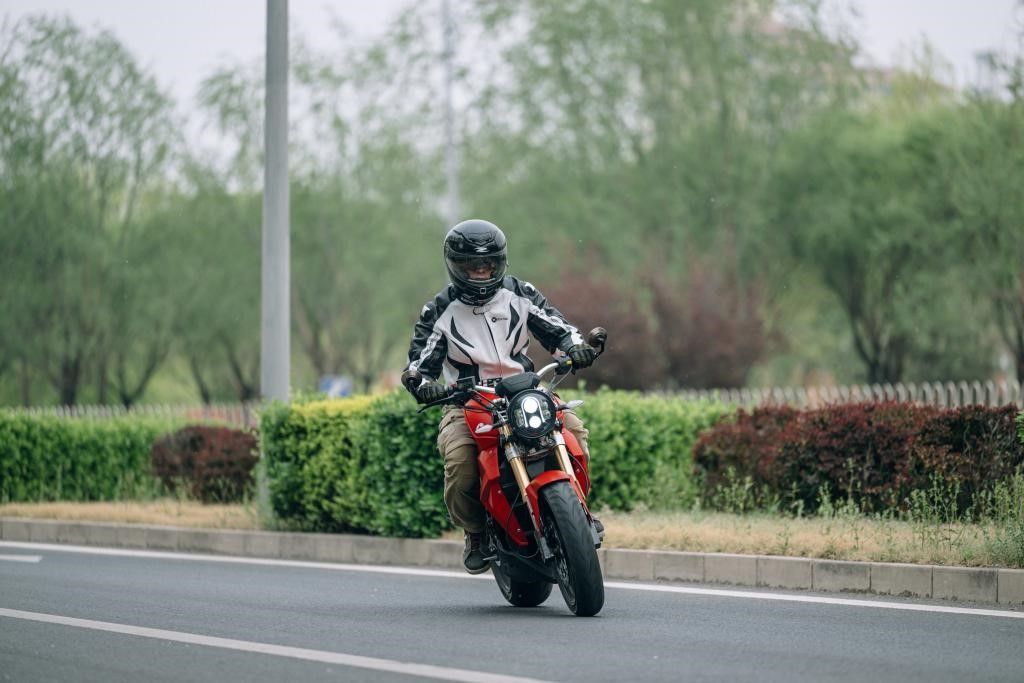 Nathan Siy is riding a red urban_classic, an electric motorcycle down a road.