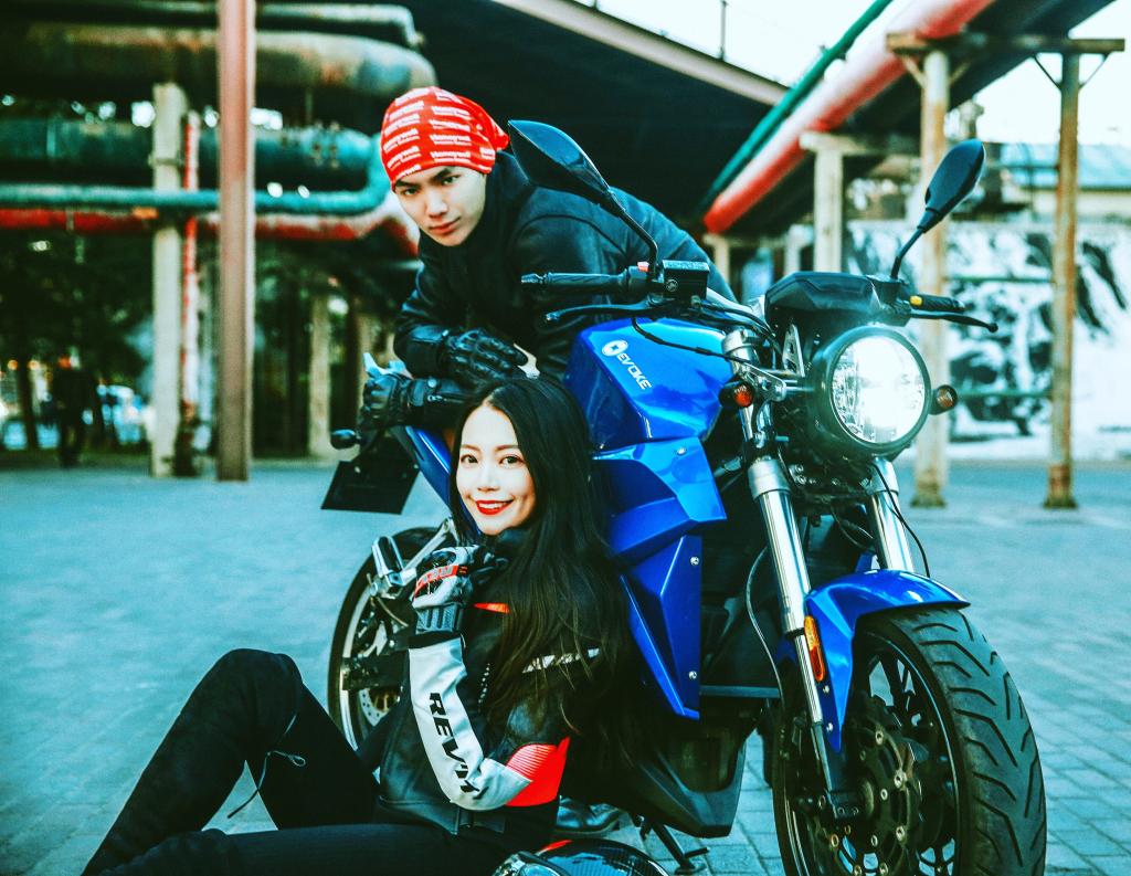 A man and a hot Asian woman are sitting on an urban classic, an electric motorcycle.