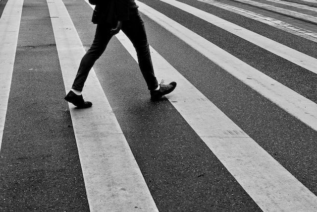 A black and white photo of a person crossing a crosswalk
