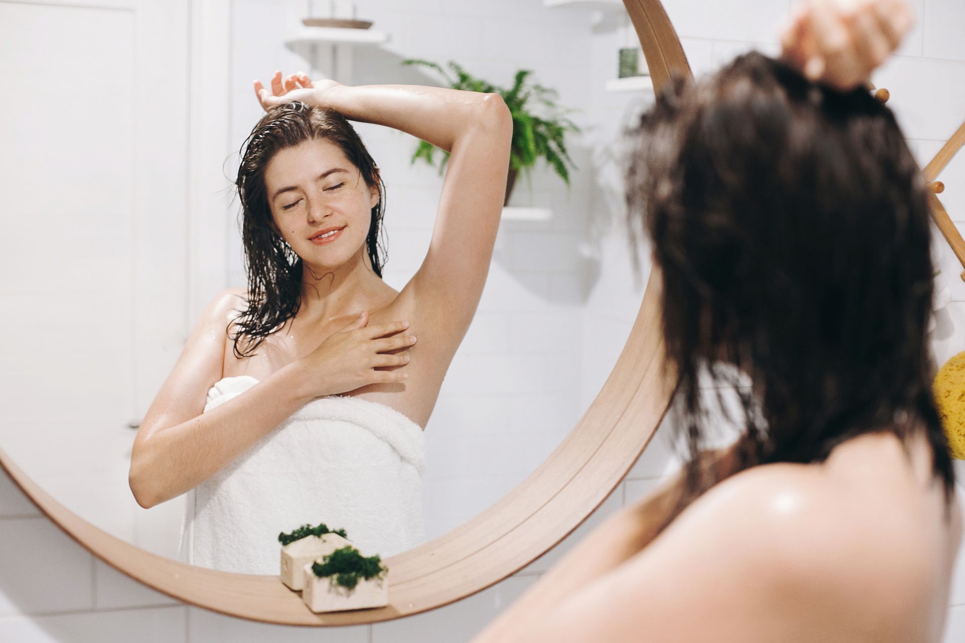 a woman wrapped in a towel looks at her reflection in a bathroom mirror
