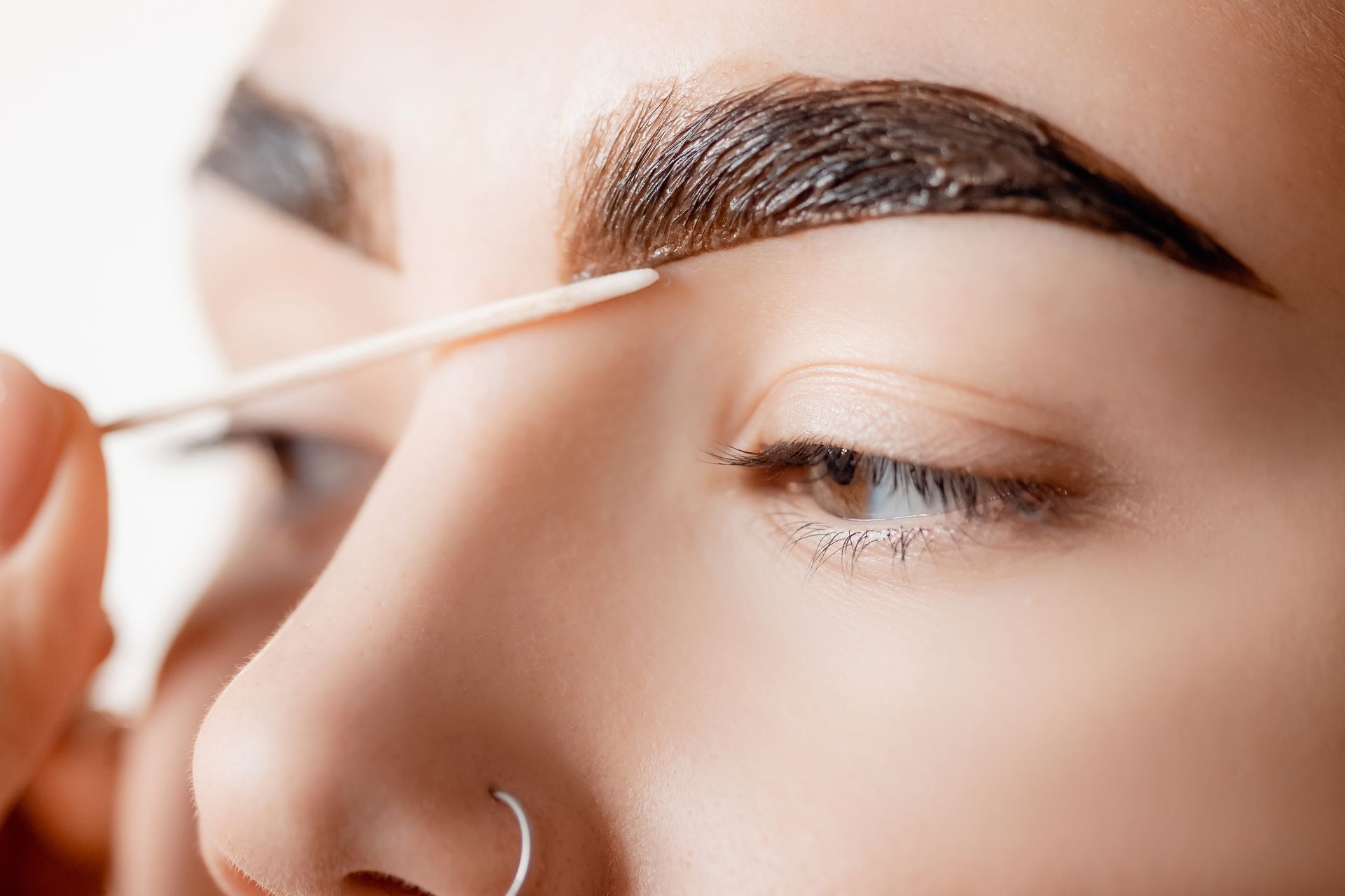a woman with a nose ring is getting her eyebrows painted