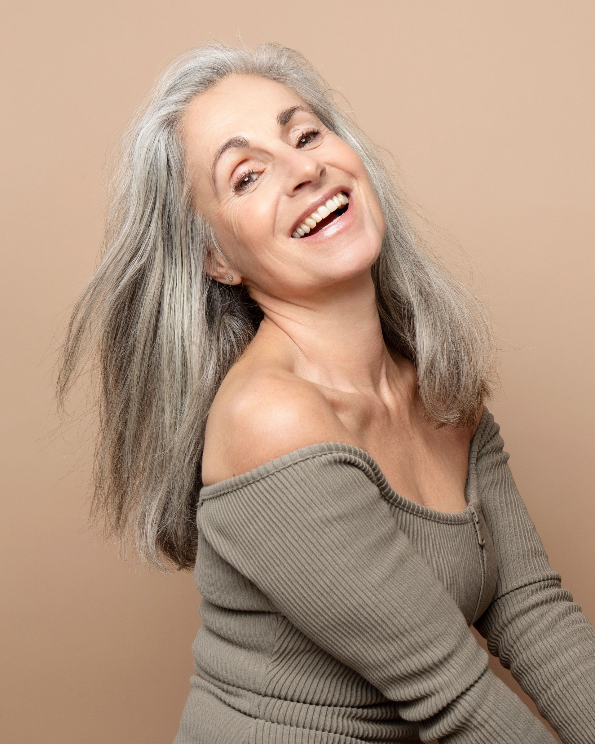 a woman with gray hair is smiling with her hair blowing in the wind