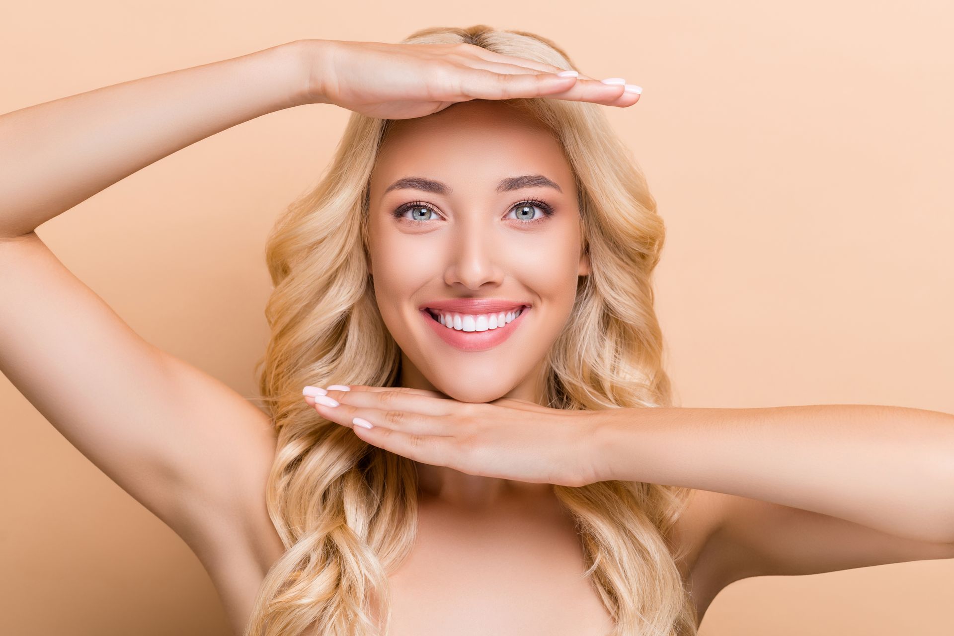 A woman is smiling and holding her hands over her face.