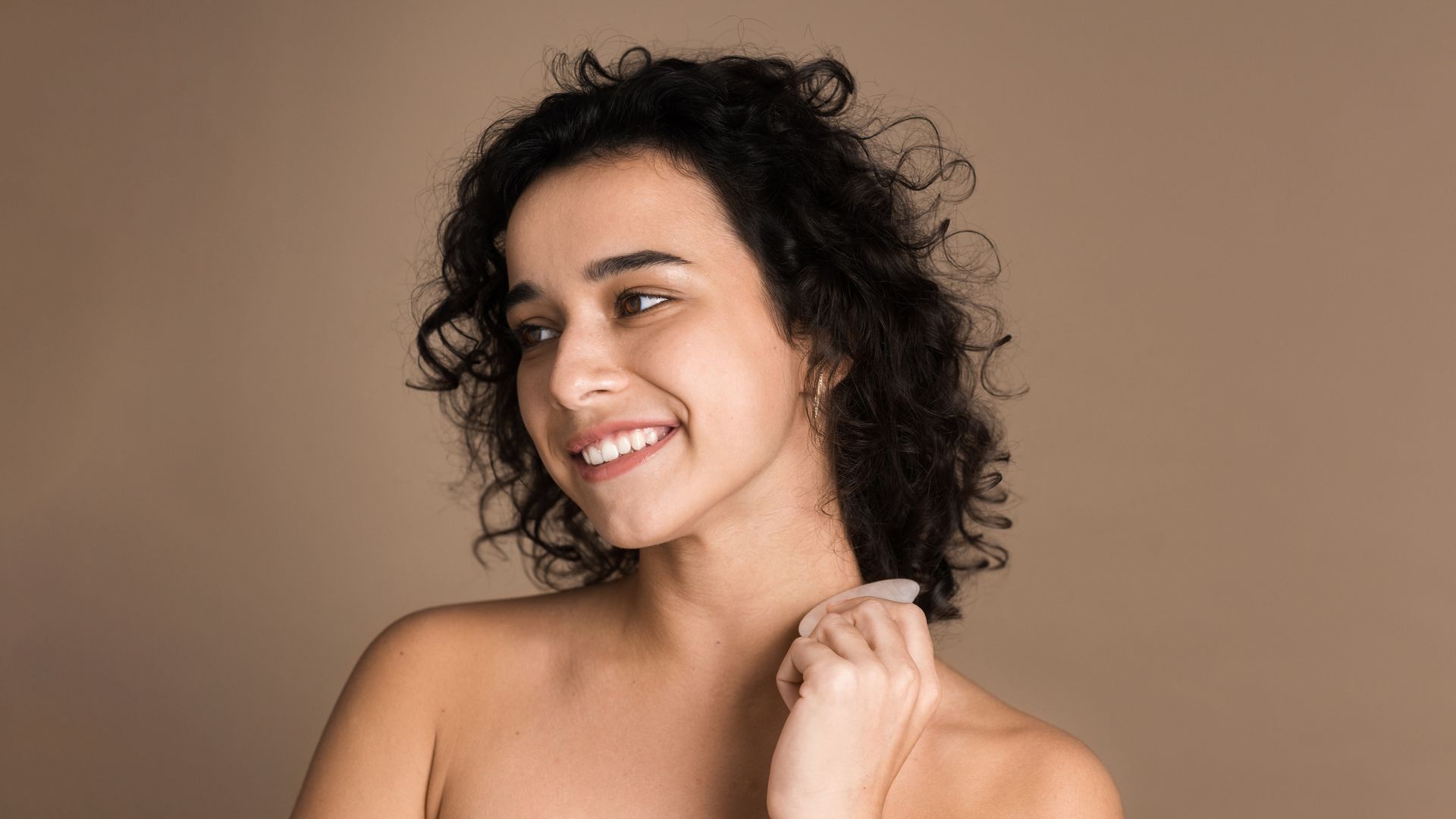a woman with curly hair is smiling and holding a white object to her neck