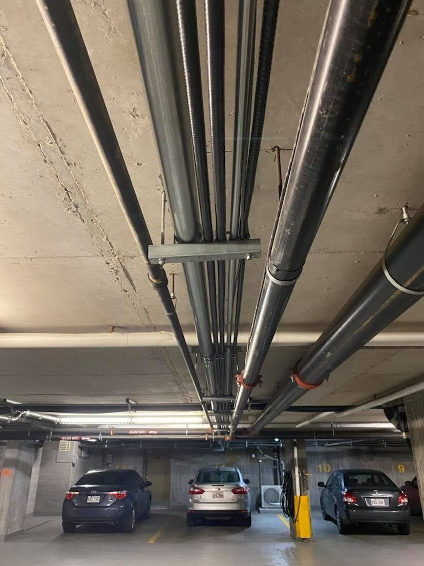 Deux voitures sont garées dans un parking avec des tuyaux suspendus au plafond.