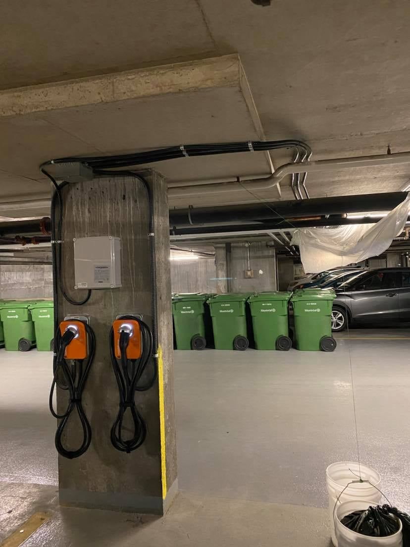 Un parking avec poubelles vertes et deux bornes de recharge.